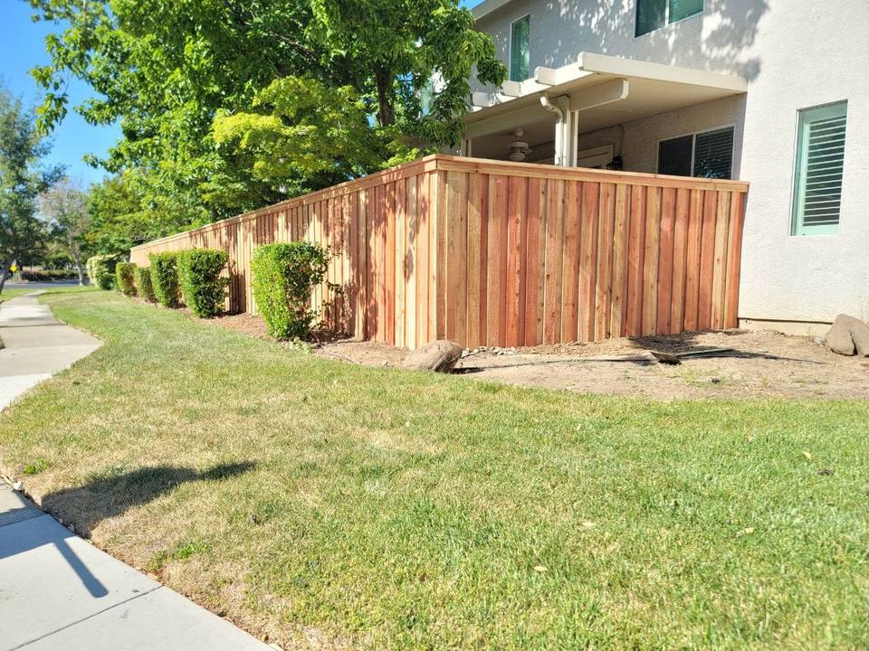 Redwood fence along a house with trimmed hedges